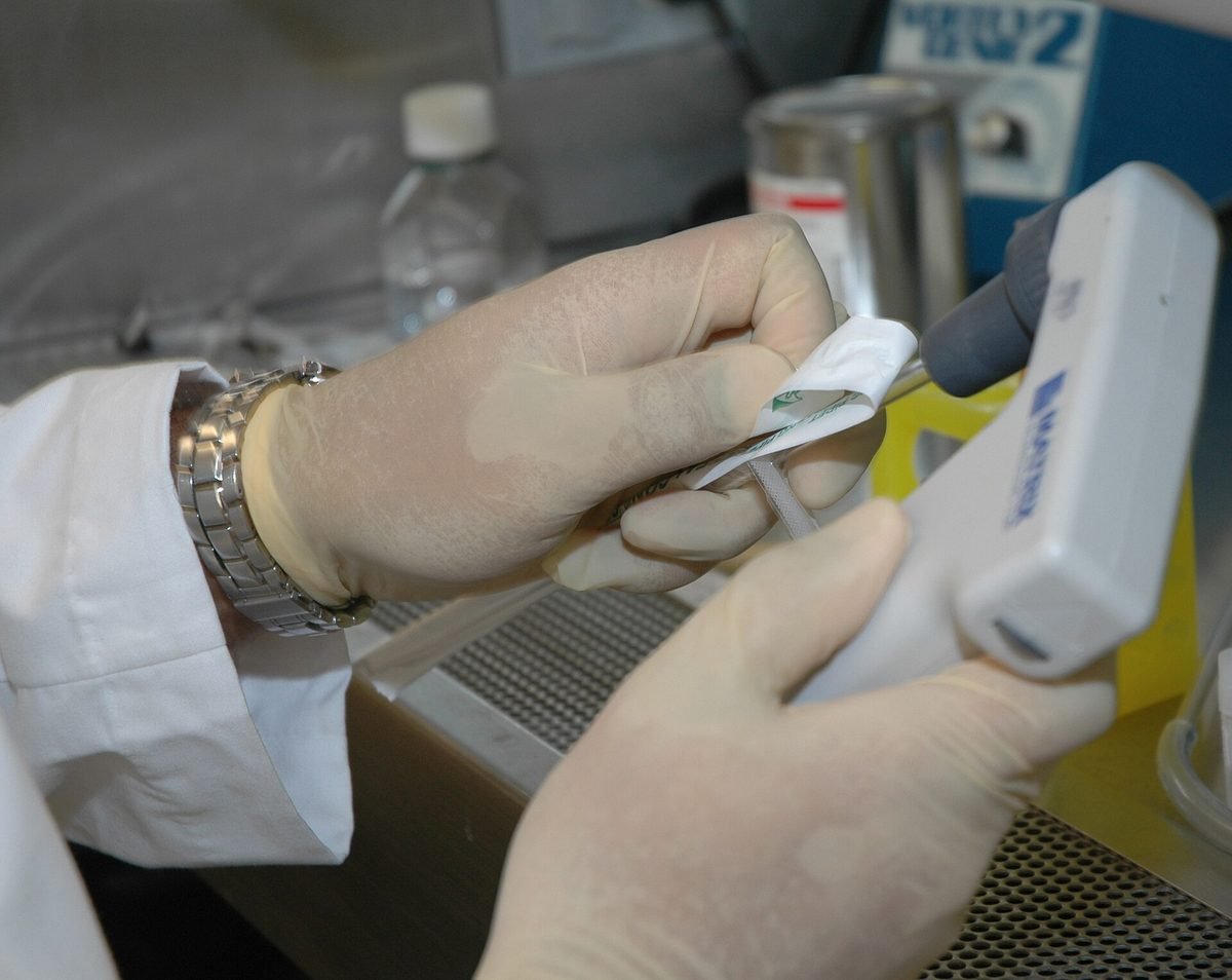 Gloved hands attaching a pipette tip in a laboratory.